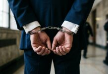 Miami Springs Resident and Coral Gables Lawyer Jackson Lainez Suspended by Florida Supreme Court Amid Lewd Conduct Charges Close-up of a man in a professional dark navy blue suit and white shirt cuffed in silver metal handcuffs behind his back.